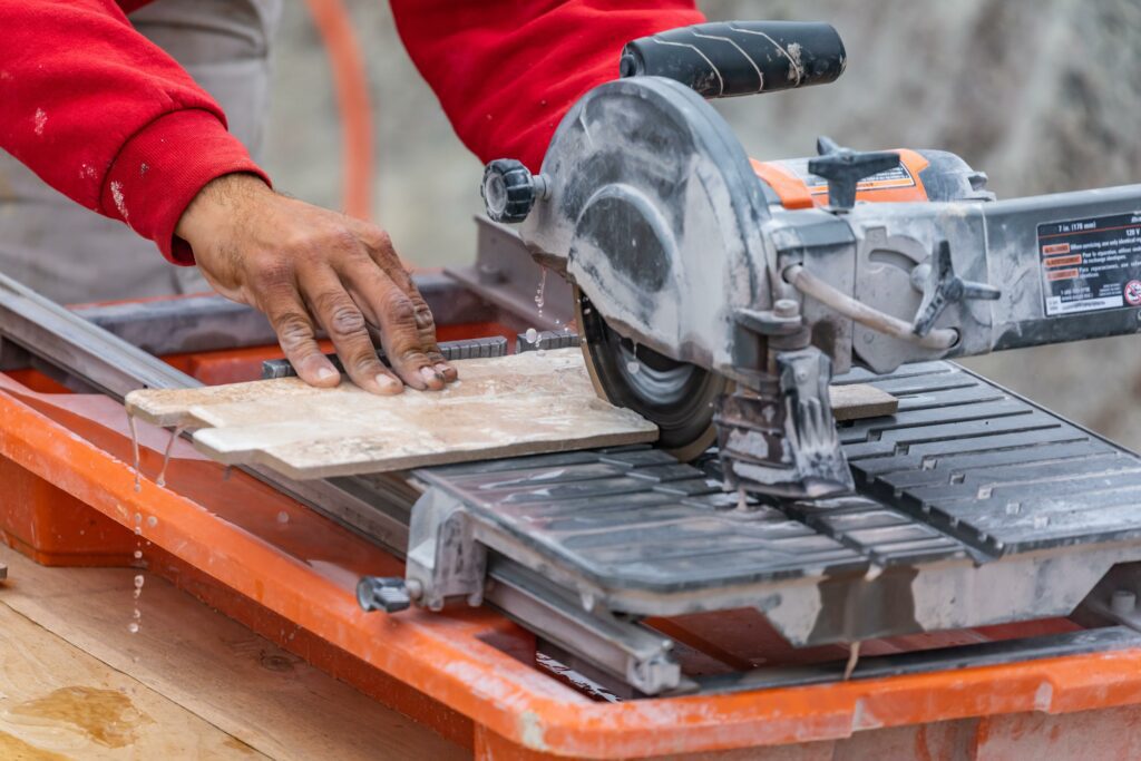 A set of hand is shown using a tile saw to cut designer ceramic tiles.